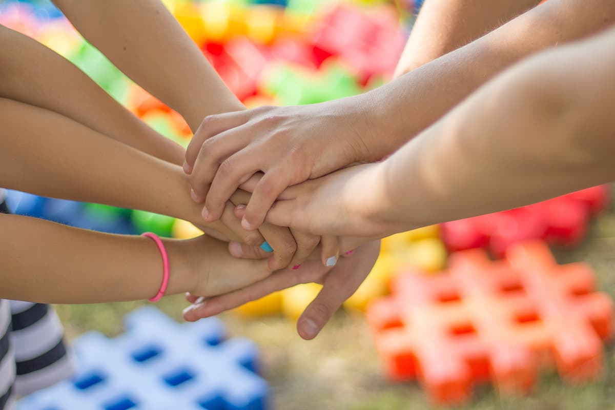 Mani sovrapposte in un gesto di unione e collaborazione, con blocchi colorati sullo sfondo