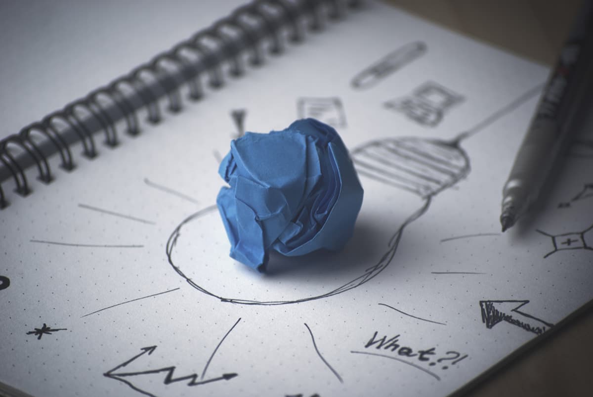 Taccuino con disegno di una lampadina e una pallina di carta blu, simbolo di un'idea creativa