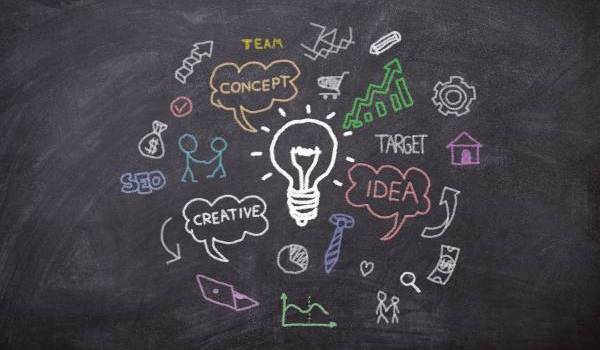 Query riuscita Gemini ha detto Illustrazione su una lavagna nera con disegni a gessetto colorato che rappresentano un brainstorming: una lampadina centrale accesa circondata da icone di business, grafici e nuvole di testo con parole come